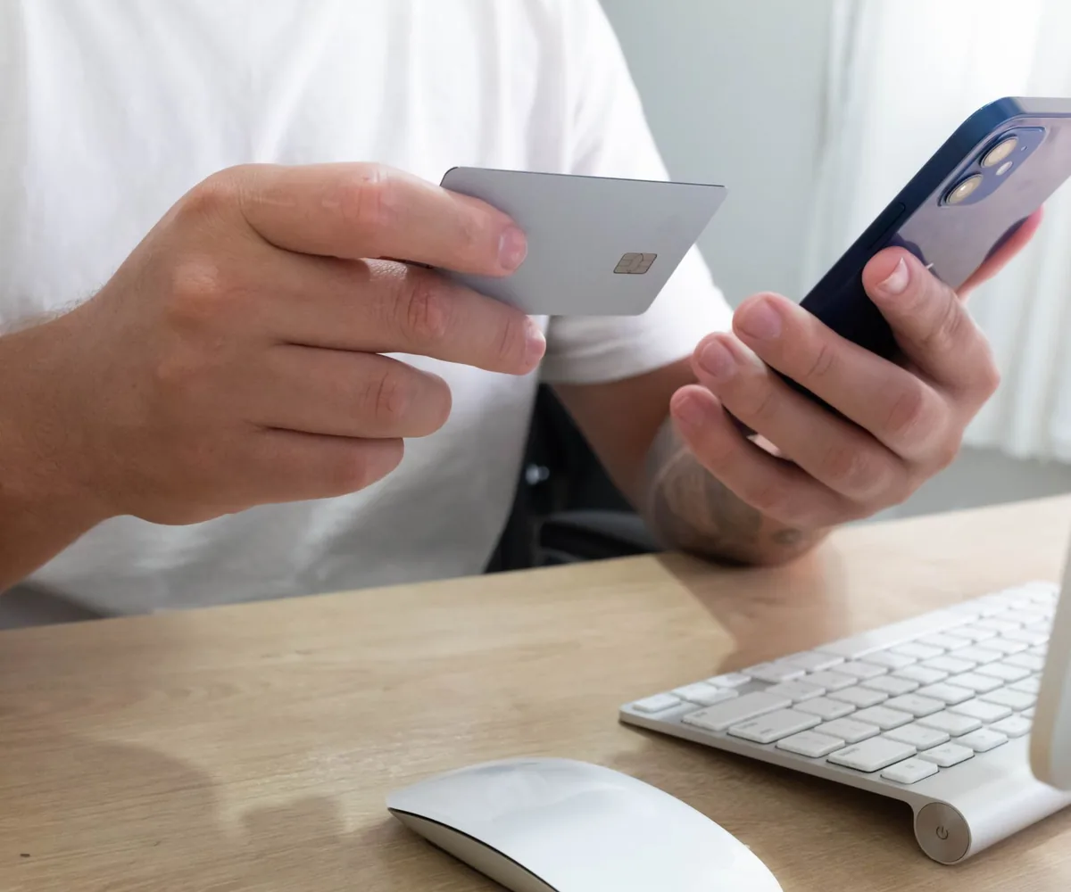 Deux mains tiennent un smartphone ouvert sur une boutique en ligne, une carte bancaire posée à côté